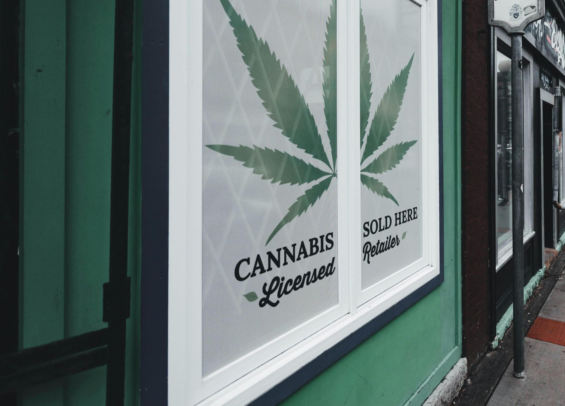 Street view of licensed cannabis retailer sign in urban setting with storefronts and cars.