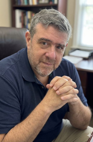 Happy man wearing glasses working remotely on laptop in modern office environment.