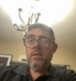 Happy man wearing glasses working remotely on laptop in modern office environment.